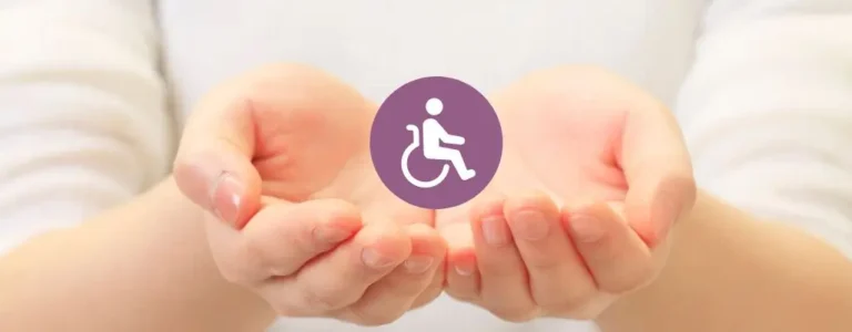 Obrazek wyróżniający do artykułu - co daje orzeczenie o niepełnosprawności. Na zdjęciu widzimy dwie dłonie złączone razem w kształt miseczki, trzymające między nimi fioletowy znaczek z białym symbolem osoby na wózku inwalidzkim. Dłonie są kobiece, z delikatnie pomalowanymi paznokciami, otoczone jasnym, neutralnym tłem. Zdjęcie to może symbolizować opiekę, ochronę oraz wsparcie dla osób niepełnosprawnych. Obraz przedstawiający symbol niepełnosprawności trzymany delikatnie w dłoniach może również sugerować odpowiedzialność społeczeństwa za zapewnienie równych praw i możliwości dla wszystkich osób, bez względu na ich fizyczne ograniczenia.