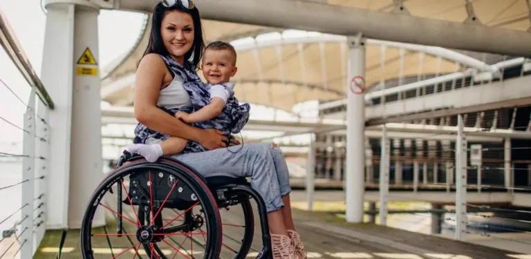 Obrazem wyróżniające do artykułu - dofinansowanie do opieki nad osobą zależną. Widoczna kobieta na wózku inwalidzkim z dzieckiem na kolanach