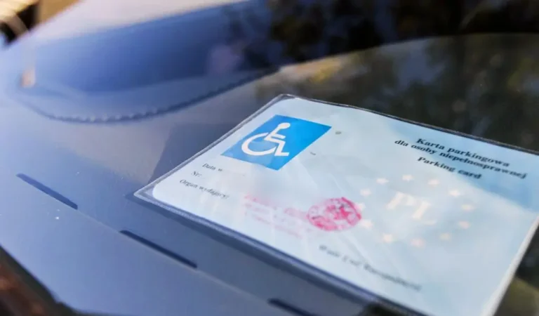 Obrazek wyróżniający do artykułu - jak uzyskać kartę parkingową dla niepełnosprawnych. Na zdjęciu widzimy kartę parkingową dla osoby niepełnosprawnej umieszczoną na desce rozdzielczej samochodu. Karta jest wyraźnie widoczna przez przednią szybę pojazdu. Zdjęcie ma charakter informacyjny, przedstawiając jak wygląda karta parkingowa dla osoby niepełnosprawnej, kiedy jest umieszczona w samochodzie.